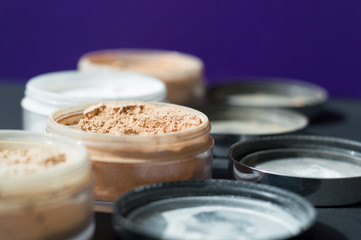 Mineral make up powder for matt skin. Variety of containers with beige and white powder for facial care. Focus on beige powder