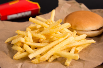 Fried potatoes and burger on brown paper. Red packet in the background