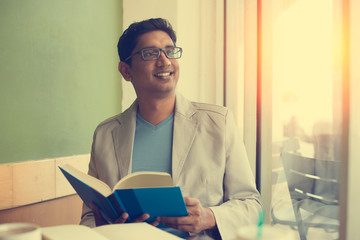 indian male reading book at cafe