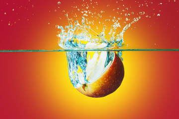 Apple slice  falling in water over bright yellow-red background