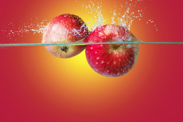 Apples falling in water over bright yellow-red background