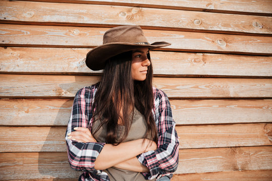 Beautiful young woman cowgirl in hat standing with arms crossed