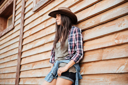 Attractive young womna cowgirl in hat standing near the house