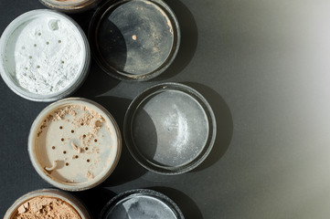Background with mineral make-up powder for matt foundation of white and beige colors on black surface