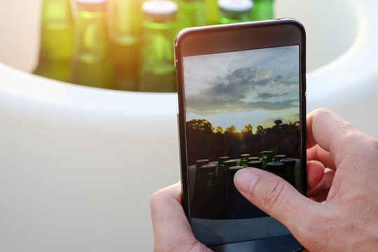 Hands of men are using mobile smart phones. Shooting bottles of beer at sunset.
