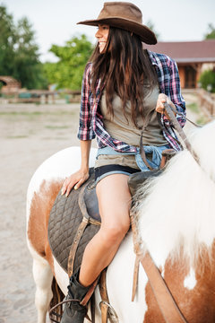 Happy lovely young woman cowgirl riding horse on ranch