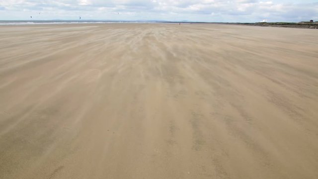 A moving carpet of sand blowing along the top of a beach on a windy day at Rest Bay in Wales, UK