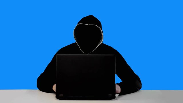 Anonymous hacker in black hood with a laptop