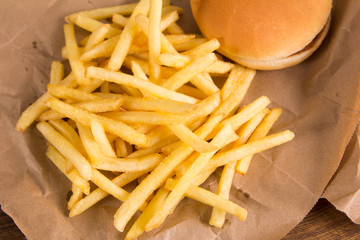 Fried potatoes and burger on brown paper. Red packet in the background