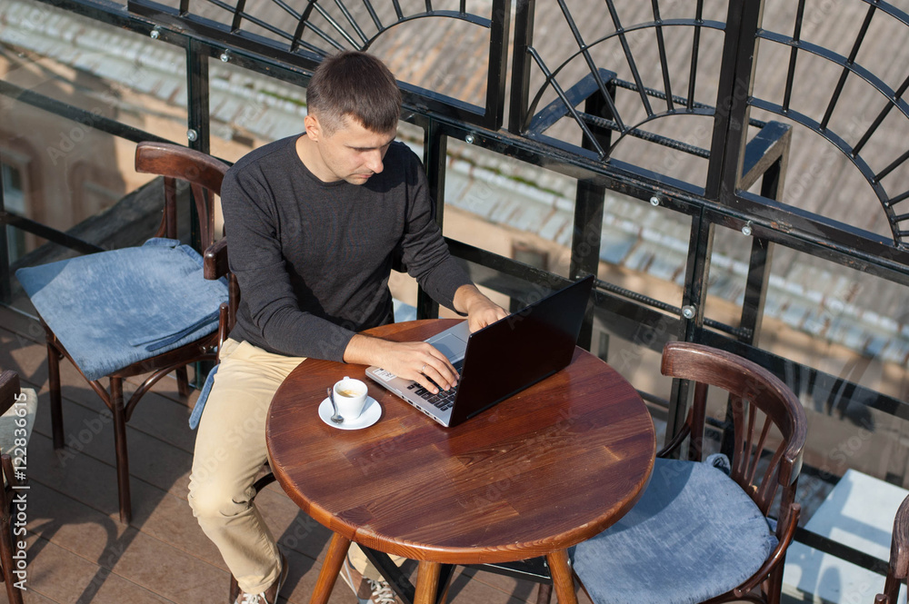 Wall mural man with a laptop sitting at a table outdoors.