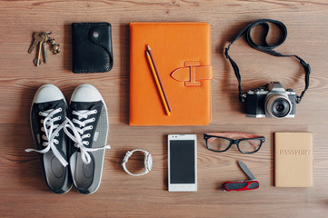 Outfit of traveler, student, teenager, young woman or guy. Objects on wooden background. Keys, camera, smart phone, glasses, passport, digital tablet, wallet, folder, watch, gumshoes.