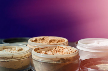 Variety of beauty containers with mineral make-up powder for matt skin on purple and pink background