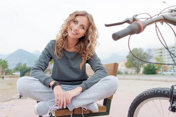 Fototapeta na wymiar Spring mood! Lovely smiling young woman with curl long hair sitting on the bench outdoors.
