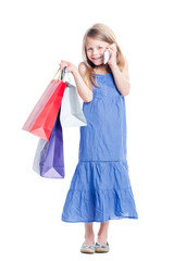 Little gossip girl. Full length of cute girl holding shopping bags and talking by smartphone. Isolated on white.