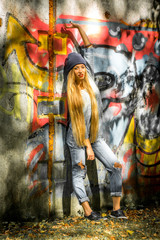 Fashionable girl with long blond hair in stylish clothes standing on a background of graffiti