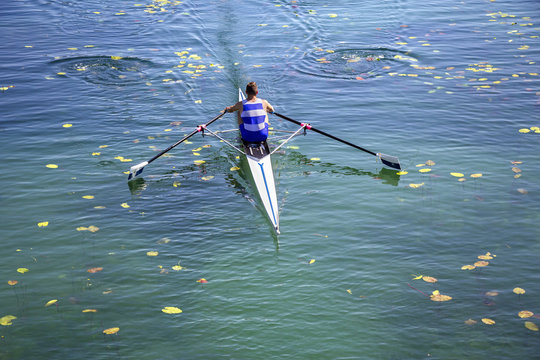 A Young single scull rowing competitor paddles on the tranquil