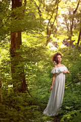 Gorgeous woman in long white dress in fairytale sunny forest
