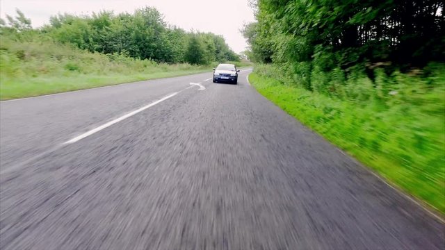 A low angle from a stabilised camera of a car driving fast along country roads in the UK.