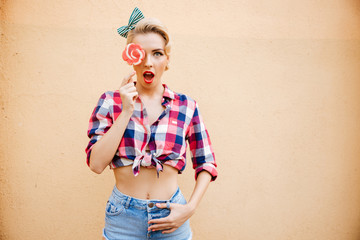 Surprised cute pinup girl covered her eye by lollipop