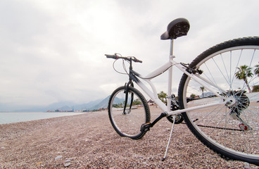 Fototapeta na wymiar Modern Bicycle parked on the sea beach with sky and mountains background