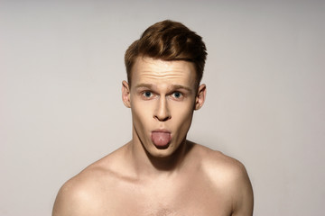 Studio fashion style closeup face portrait of young emotional man looking in camera and showing tongue