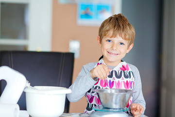Funny blond kid boy baking cake indoors
