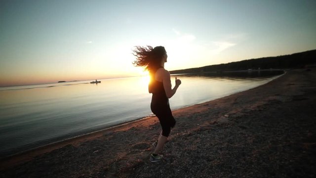 Athletic women running outdoors on promenade at sunset near ocean enjoying evening run. Evening jog along the coastline. Sports girl runs along the beach at sunset. Jogging at sunset. Healthy