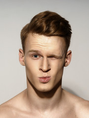 Obraz premium Studio fashion style closeup face portrait of young emotional man giving a kiss and winking
