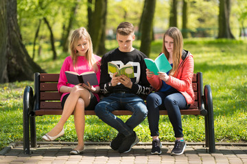 Nastoletnia młodzież czyta książki na ławce w parku