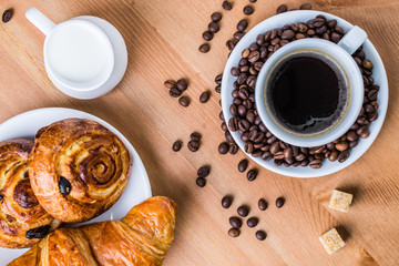 Coffee cup with cinnabon and croissant on wooden background.