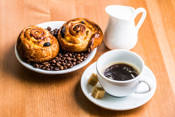 Coffee cup with cinnabon and milk jug on wooden background.