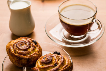 Coffee cup with cinnabon and milk jug on wooden background.