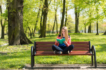 Dziewczyna czyta książkę na ławce w parku - obrazy, fototapety, plakaty