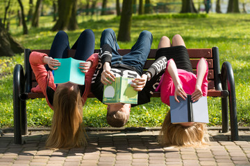 Młodzież czyta książki w parku na ławce - obrazy, fototapety, plakaty