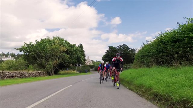 A group of cyclists riding around a corner along country roads in the English countryside in the UK on a sunny day. Taken with a Steadicam