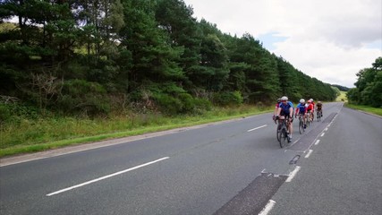 A side view of a group of cycling athletes out on a training ride on the country roads in the UK countryside on a sunny day. 