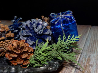 новогодние украшения, подарок и елочные шишки лежат  на черном фоне     