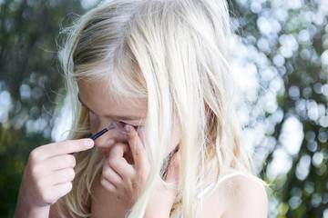 Close up portrait of adorable little child blond girl playing with mommy's make up outside 