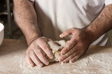 Detail on hand baker kneading dough on a black board with flour powder. The concept of baking and pastry shops.