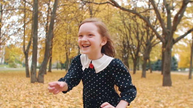 portrait cute little girl with curly hair, in dress with polka dots runing through the autumn alley in the park slow mo