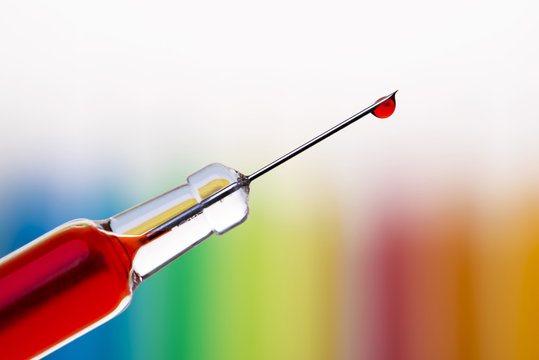 Macro of a single drop of blood hanging at the end of a syringe needle over blurred rainbow background. Shallow DOF. - Powered by Adobe