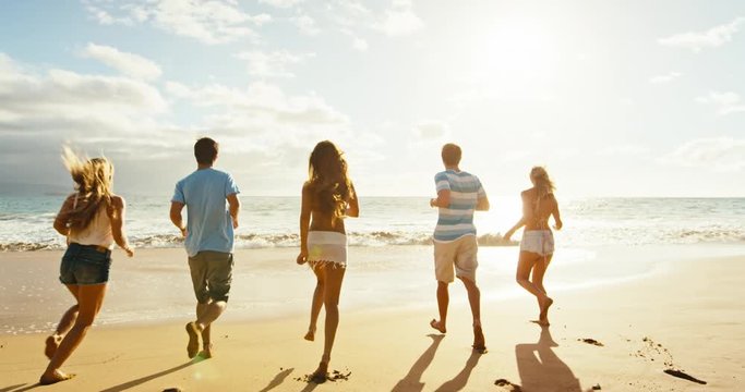 Group of friends having fun running down the beach at sunset