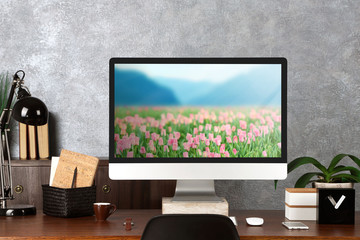 Comfortable workplace with modern computer and field of beautiful blooming tulips on screen