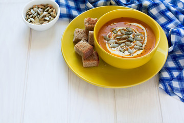 Roasted pumpkin soup with cream and pumpkin seeds on white wooden background