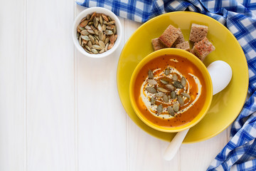 Roasted pumpkin soup with cream and pumpkin seeds on white wooden background. Top view