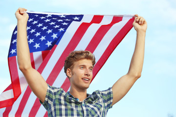 Young happy man with American flag on sky background