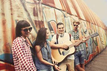 Happy friends playing guitar and singing on street