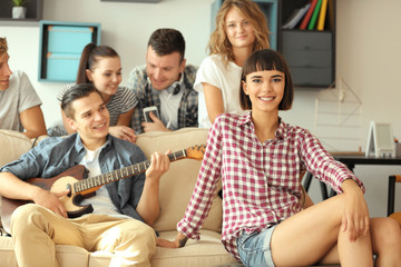Happy friends playing guitar and listening to music at home