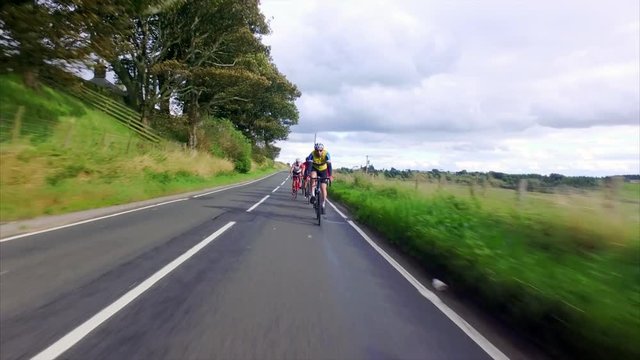A stabilised cam of a group of cycling athletes out on a training ride on country roads in the UK countryside on a sunny day. 