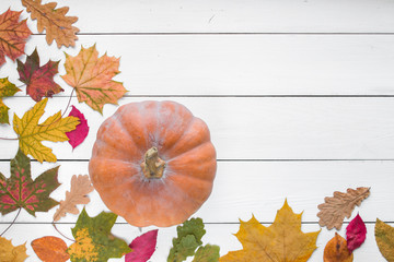 pumpkin with fallen colorful leaves on white colored wooden table, top view, 